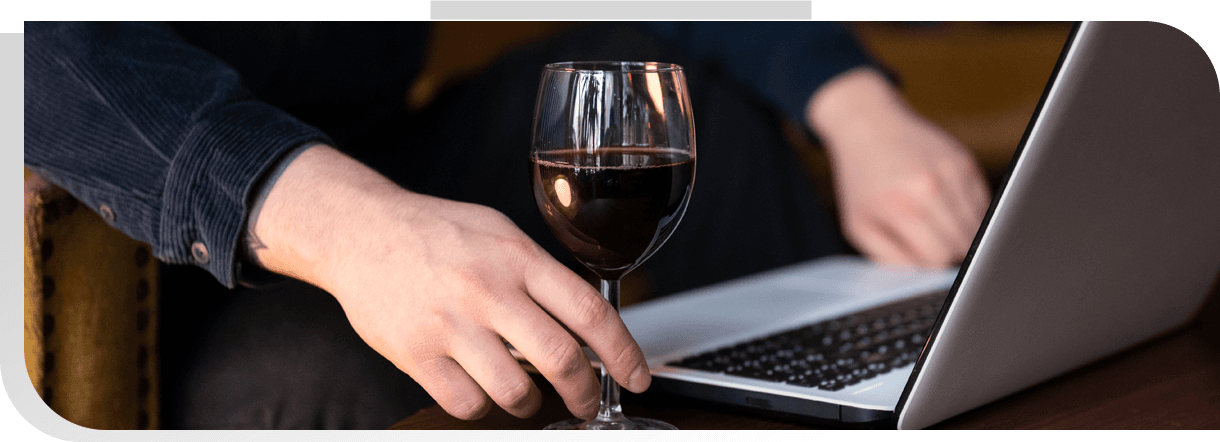 A hand with a glass of wine in front of a laptop